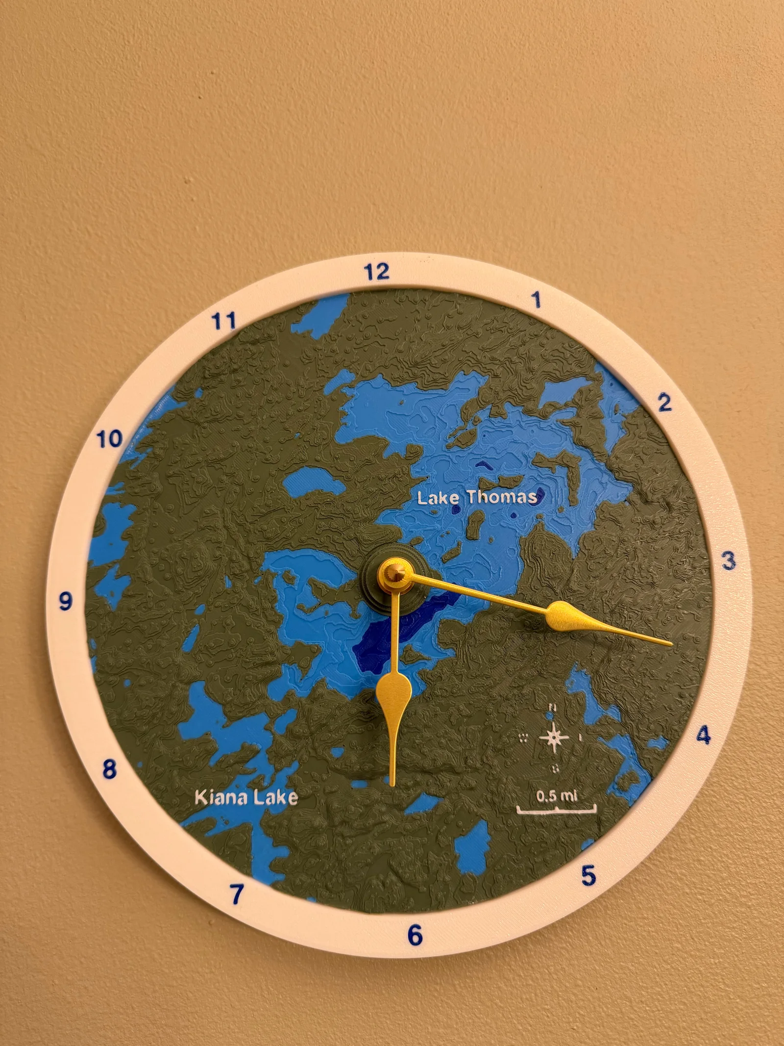 Lake Thomas topographic clock with a white rim, green terrain, blue lakes and gold hands.