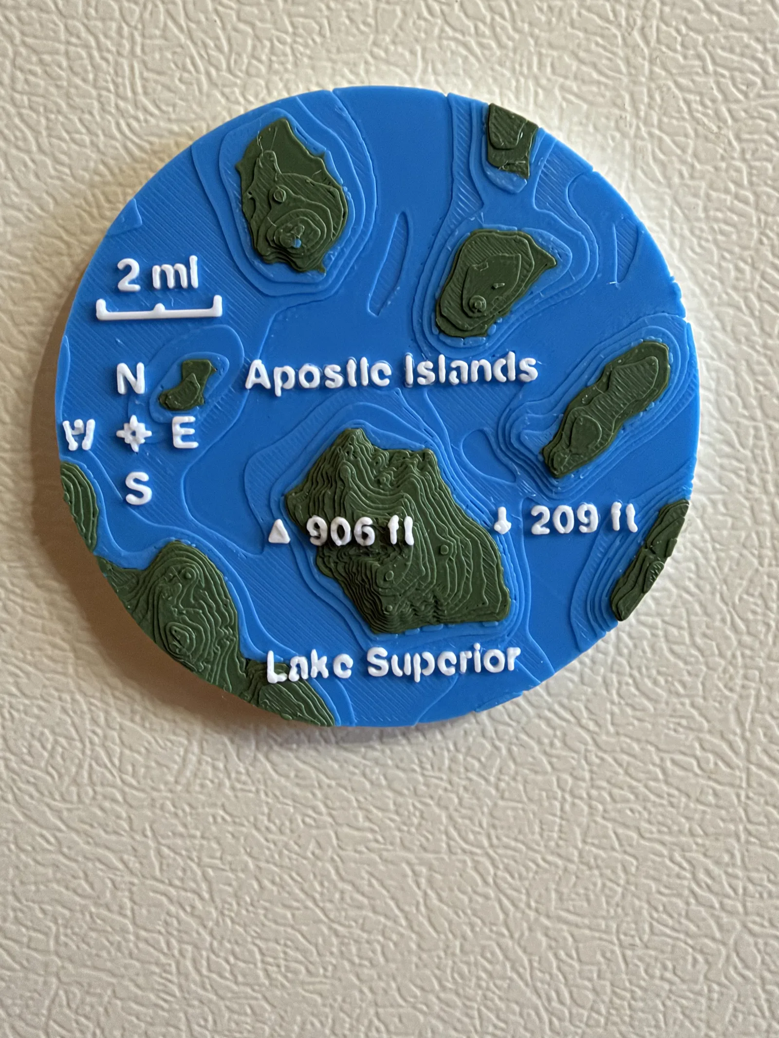 Apostle Islands magnet on a refrigerator, with blue Lake Superior depths and raised green islands.