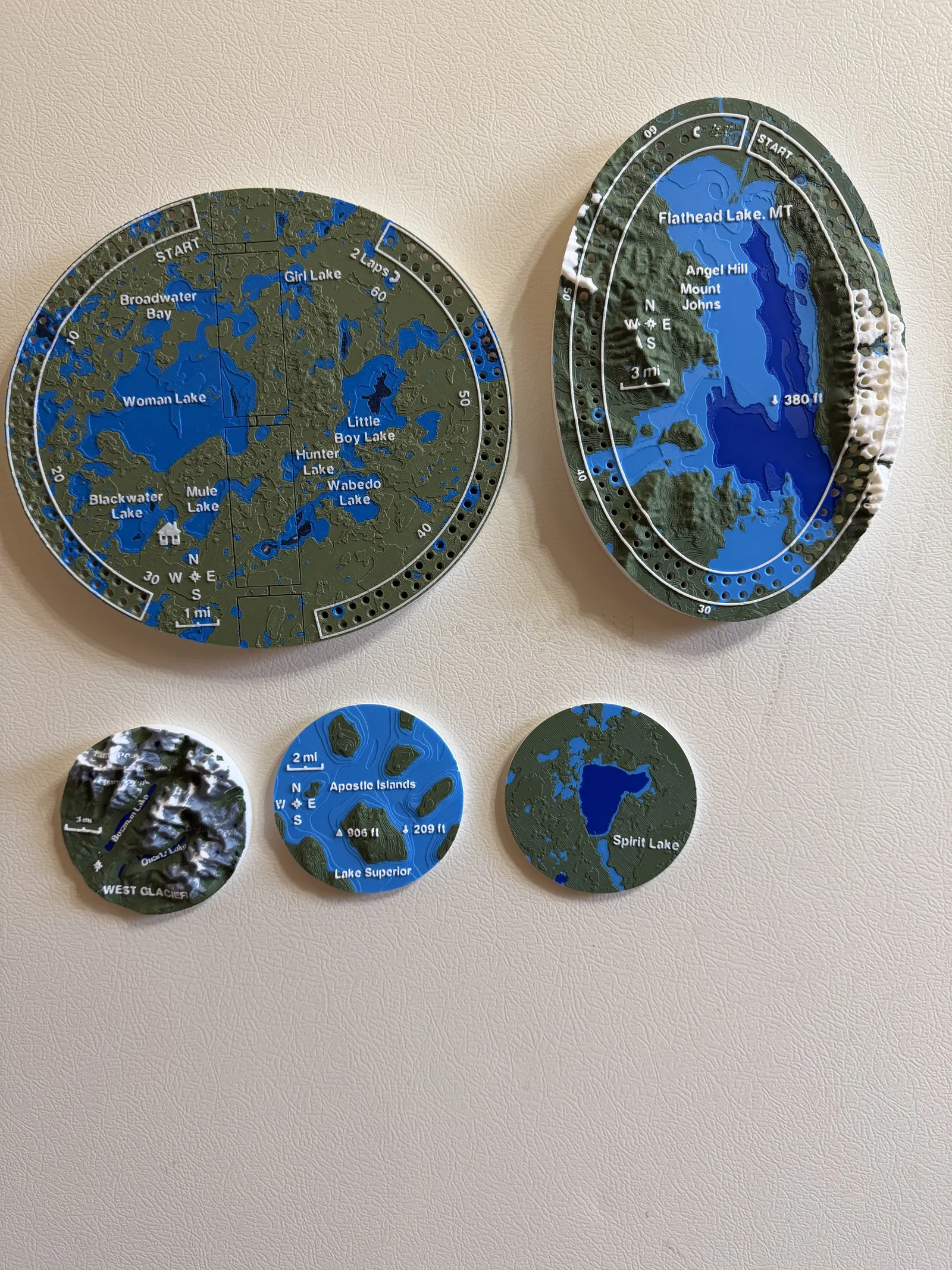 A folding Woman Lake board, an oval Flathead Lake board and three landscape magnets displayed together on a refrigerator